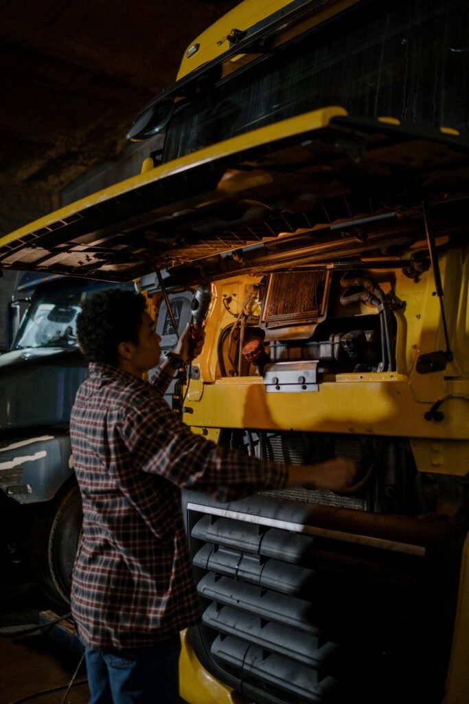 A mechanic works on a truck engine in a dimly lit garage, focusing on repairs.